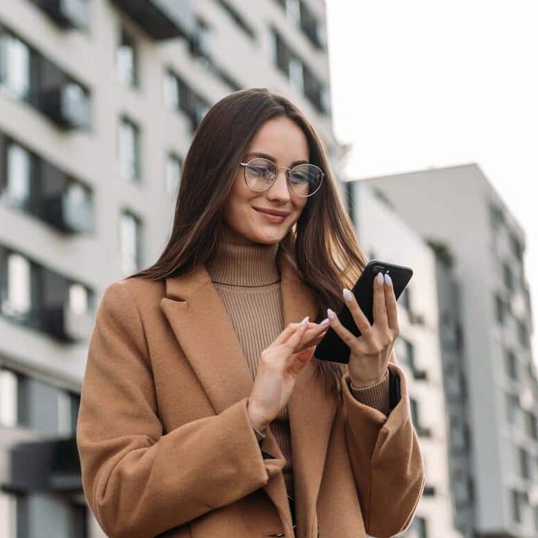 woman on city street looking at phone and smiling